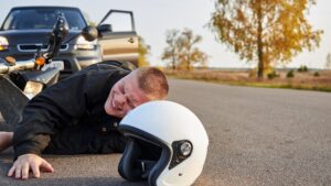 Motorcycle rider lying in the road in pain due to accident.