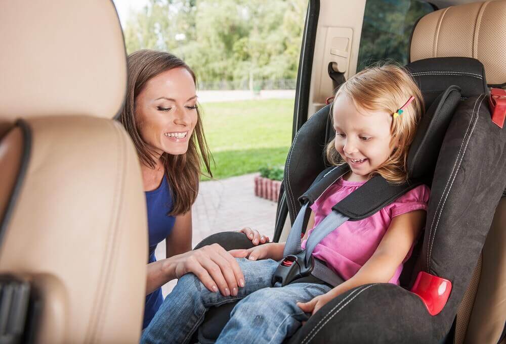 Mother putting cute girl on a car seat for safety.