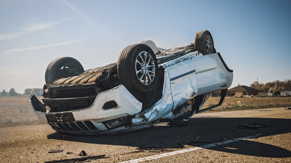 Rollover and burning car lying on its roof in the middle of the road after collision.