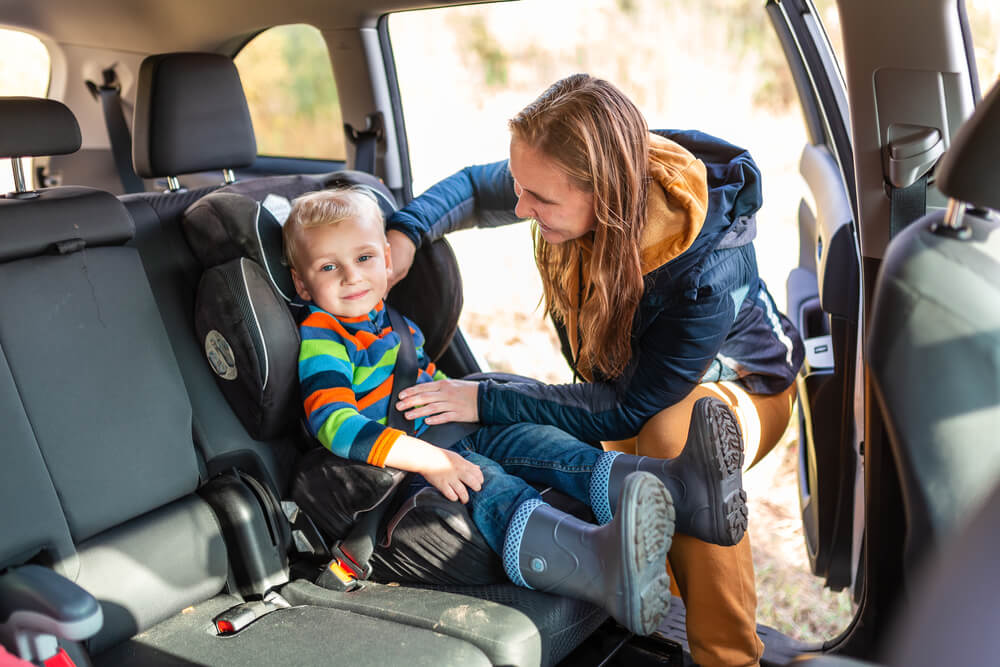 Mother fastening safety belt on booster seat for her kid.