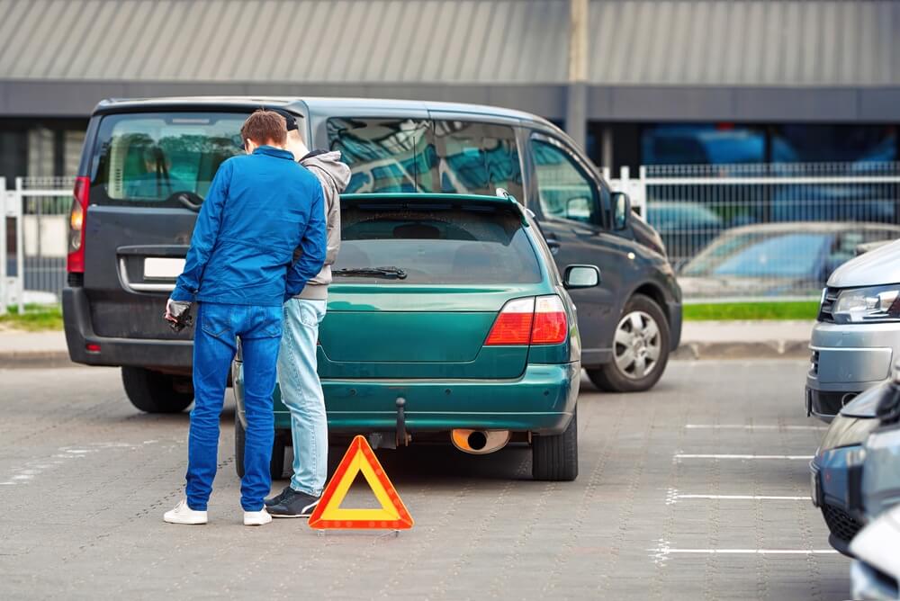 Men set up red warning triangle after collision in parking area.